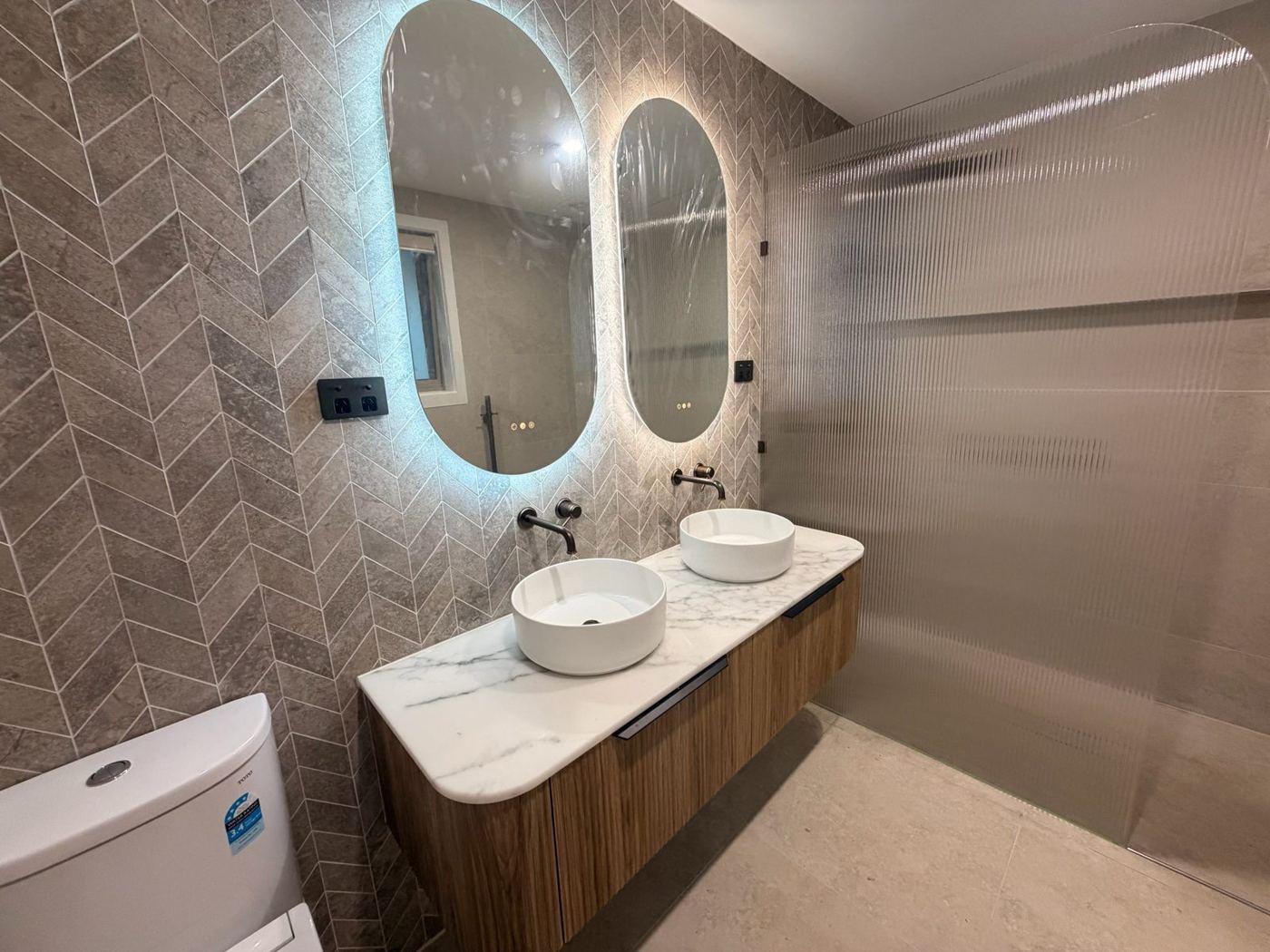 Renovated bathroom with herringbone tiles and backlit mirrors