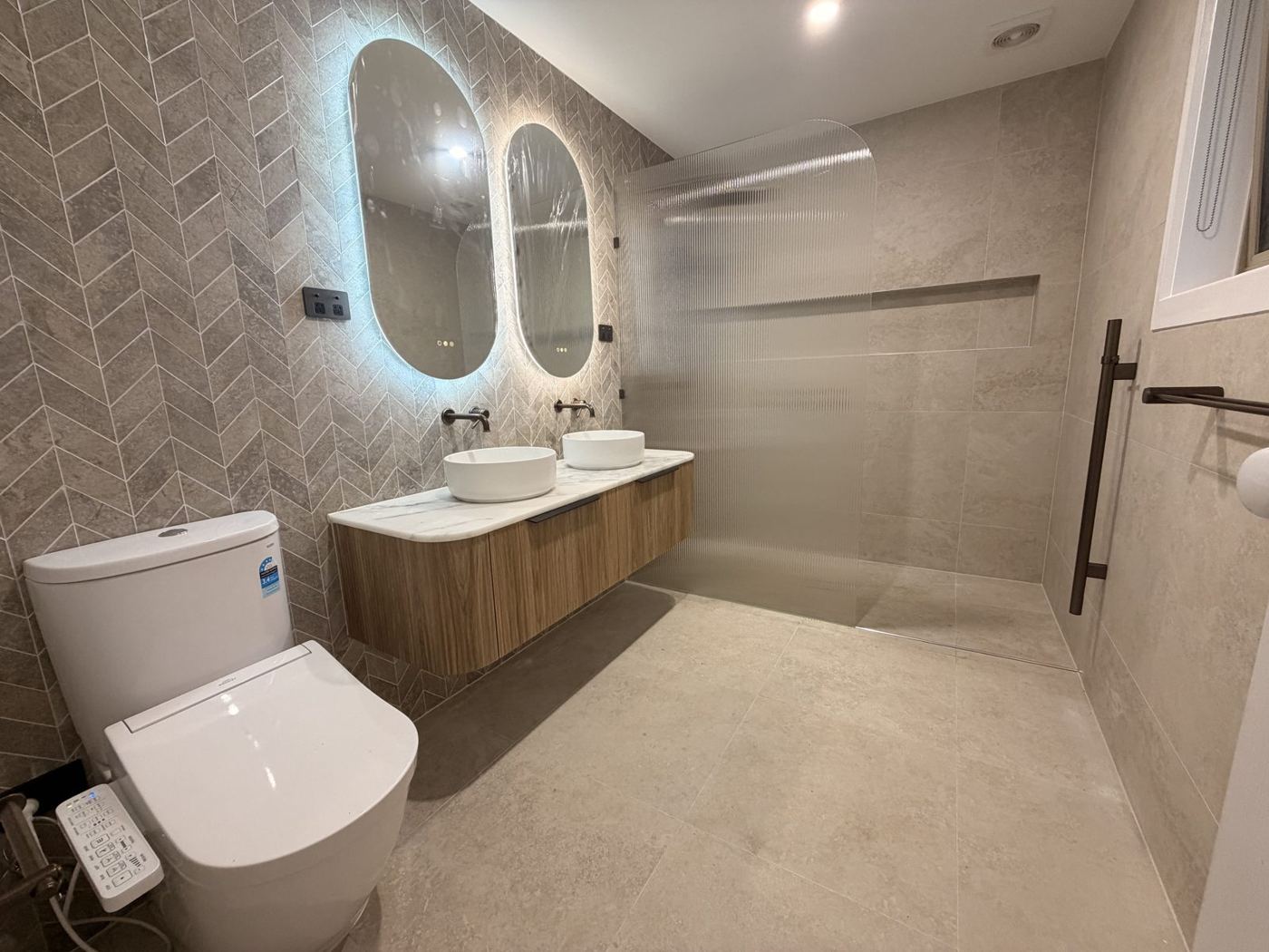 Renovated bathroom with backlit mirrors, double vanity and walk-in shower